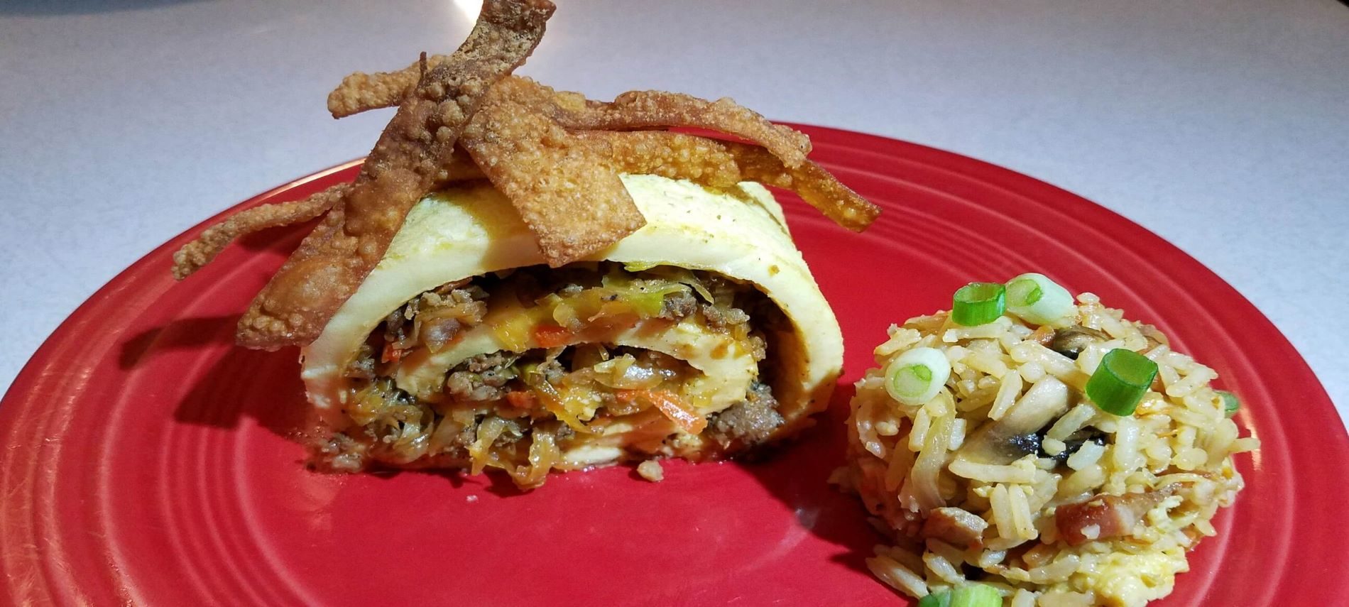 rolled omelet with egg roll meat and veggie filling with a side of fried rice on red plate
