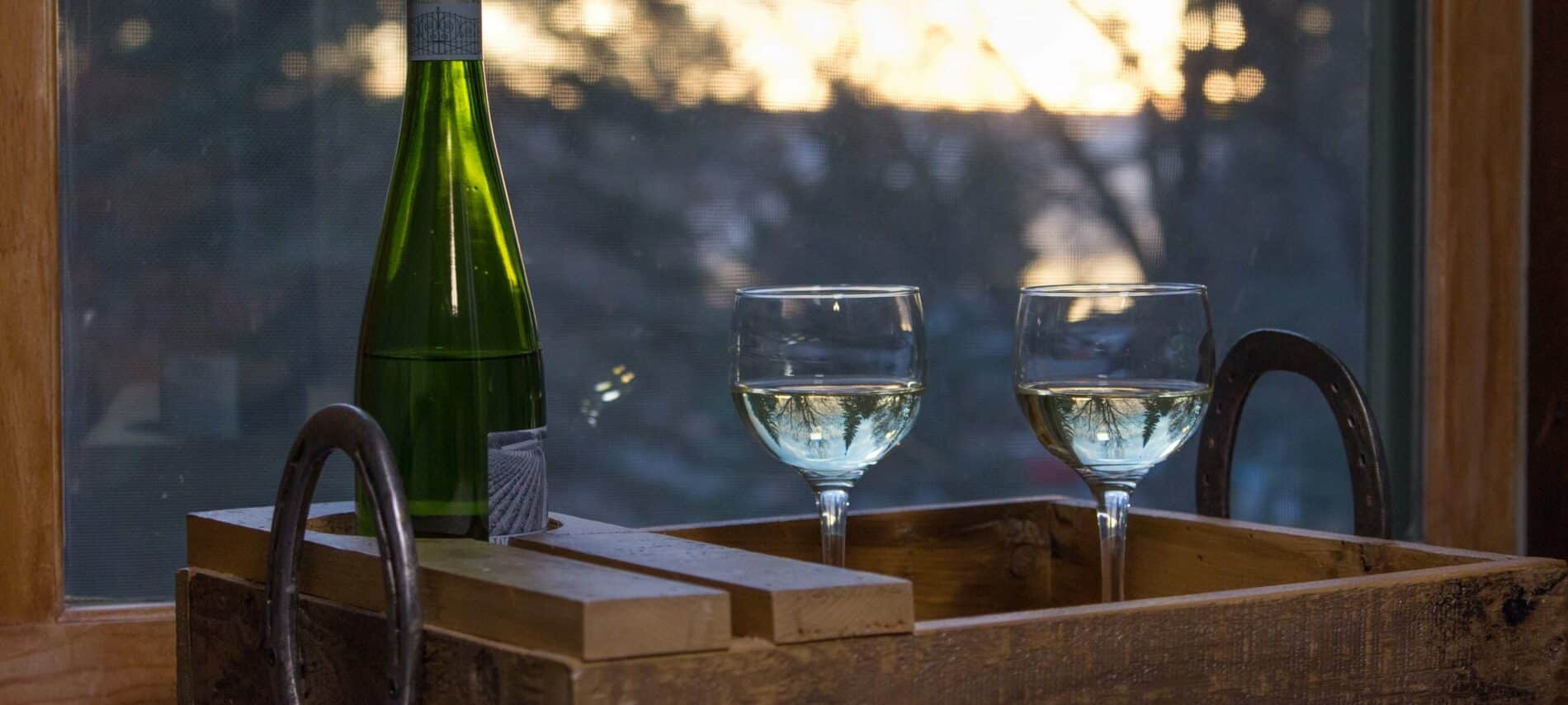 brown wooden tray with wine glasses and wine in front of window overlooking sunrise