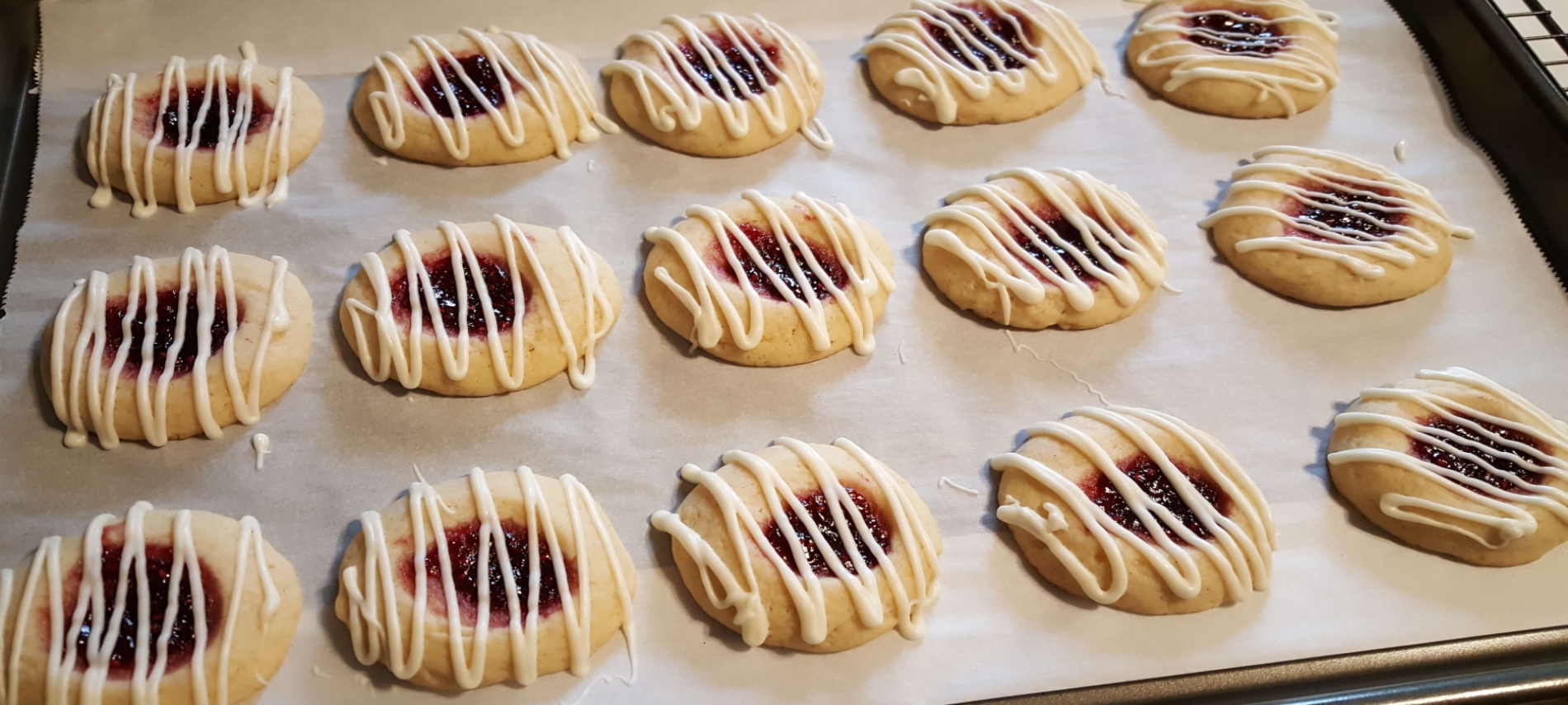 butter cookies with raspberry jam and white chocolate drizzle on parchment paper