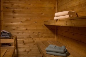 interior of sauna with wood siding, two wood benches with folded blue robes and beige towels