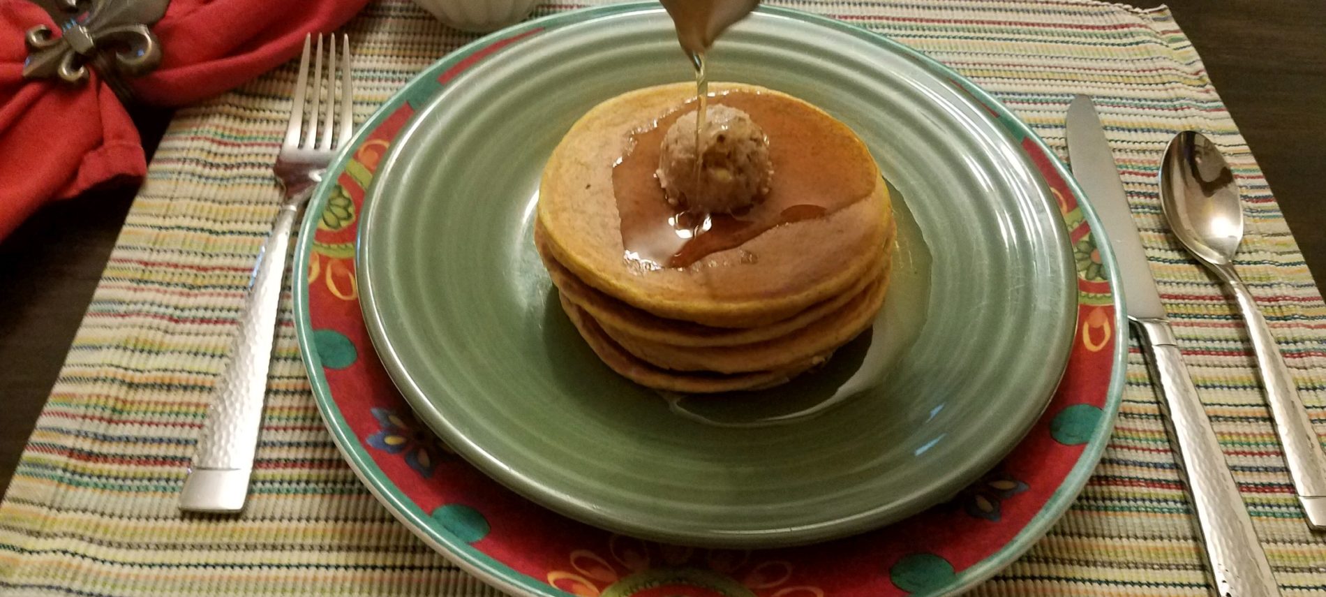 sweet potato pancakes with pecan butter on green plate with syrup being poured on pancakes