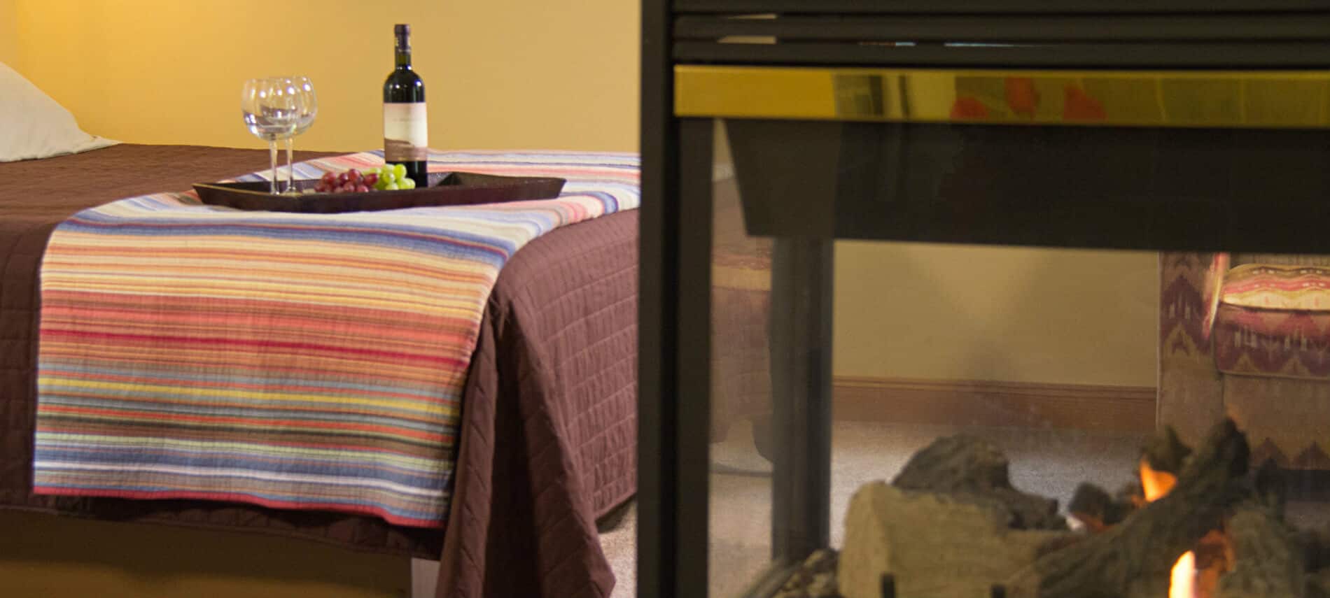 Golden painted guest room with carpet, bed topped with tray of grapes and wine, and a fireplace