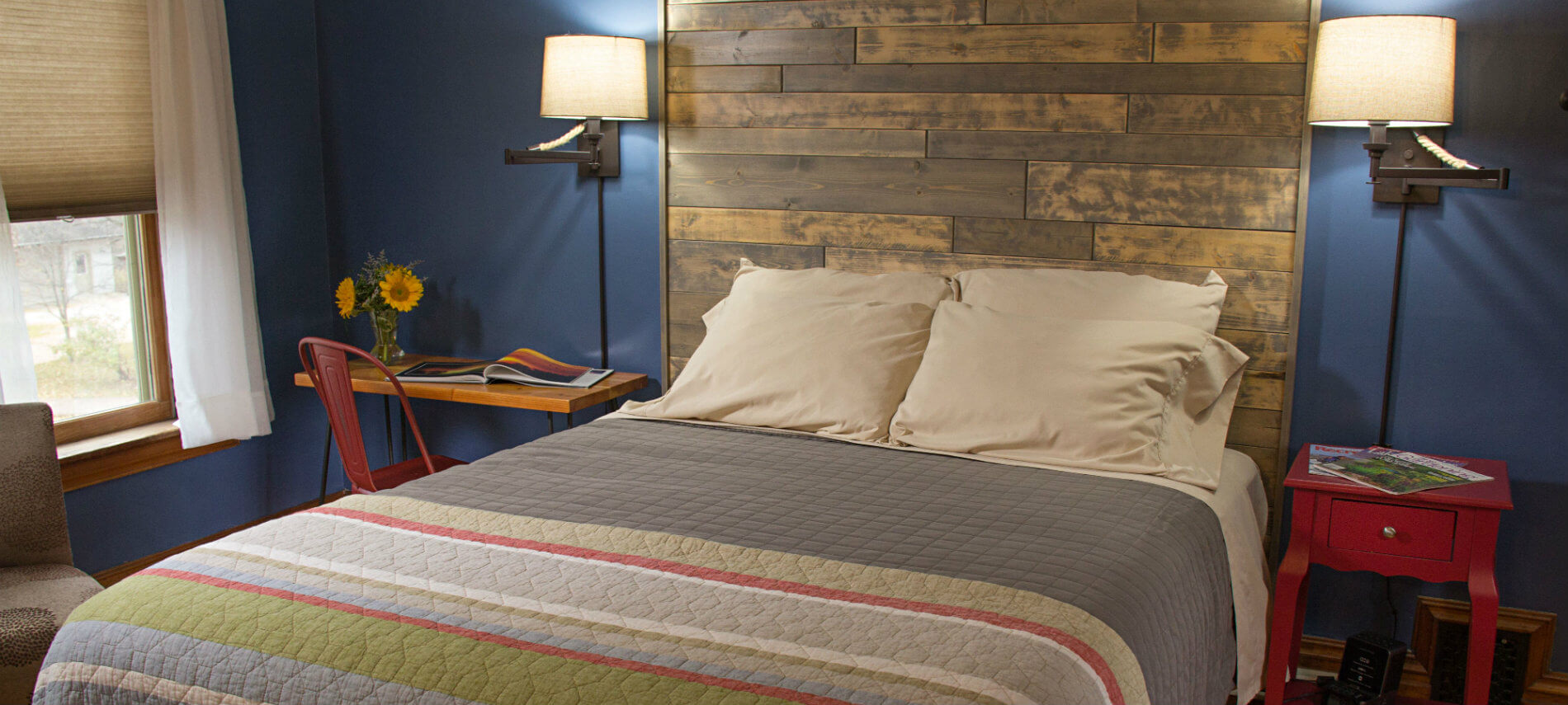 Blue guest room, bed with striped quilt and shiplap headboard, two nightstands and reading lights, and window
