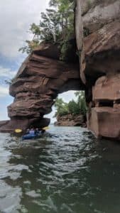 kayaker on lake superior entering brownstone arch with trees in the distance