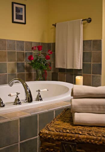 White jetted tub surrounded by tile and topped with fresh red roses, with folded and hanging tan bath towels