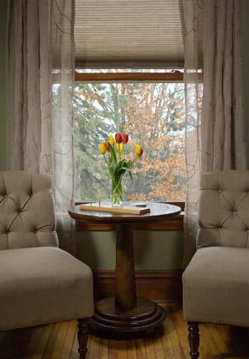 Sitting area with two upholstered chairs flanking round wood table in front of window