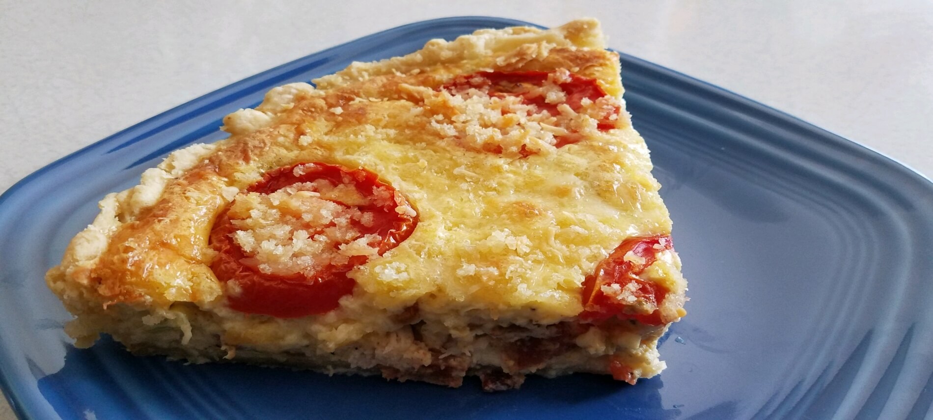 Slice of golden quiche topped with tomatoes on a blue plate